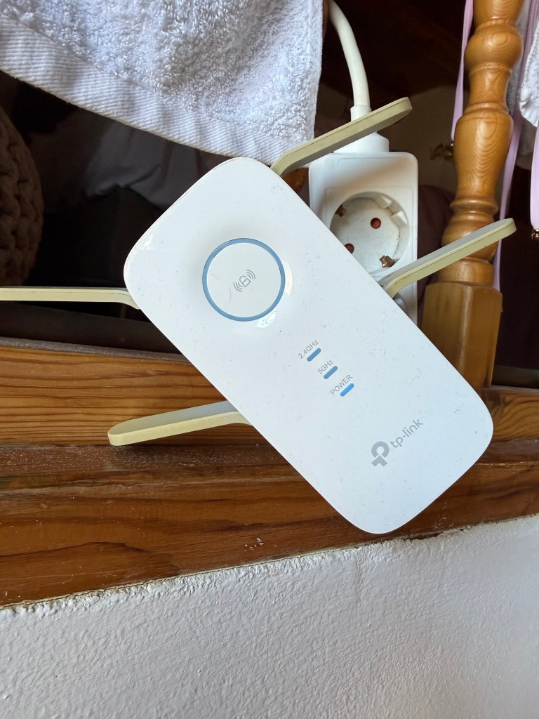 A TP-Link wireless range extender positioned on a wooden surface, with visible power and signal indicator lights.
